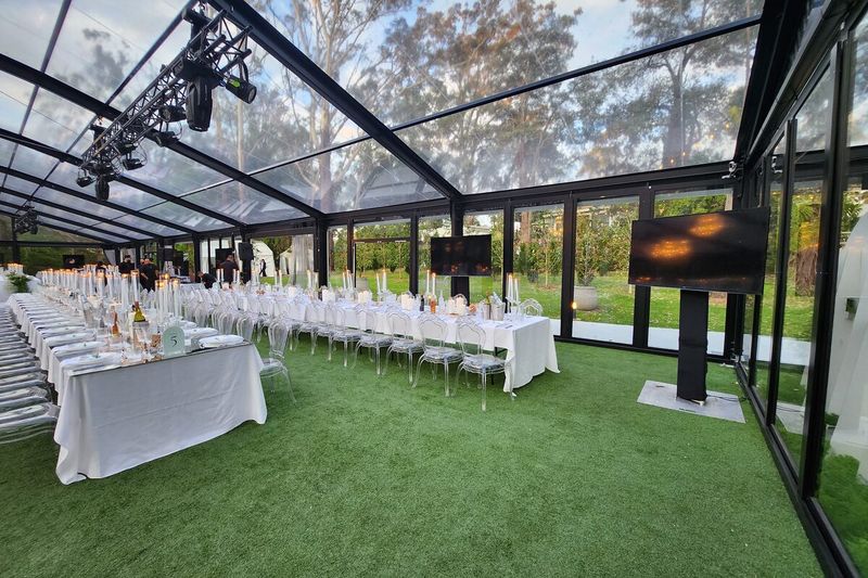 Glass marquee with long tables set on lawn and lighting rigged overhead