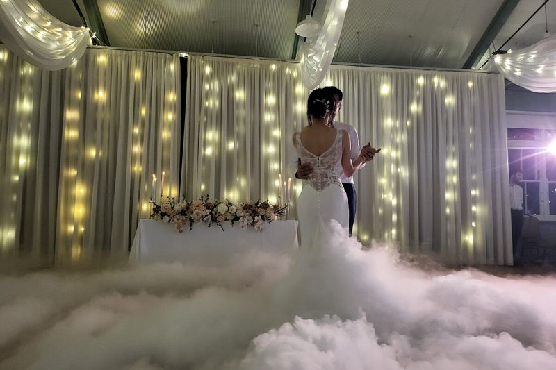 Bride dancing in a dry ice cloud against a curtain of warm fairy lights
