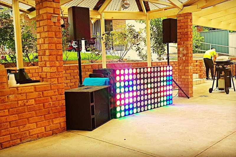 DJ set-up with an LED panel under a brick pavilion at a home party
