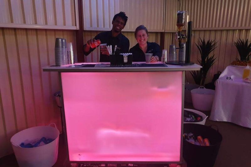 Two bartenders working behind the glow bar lit pink at a private function