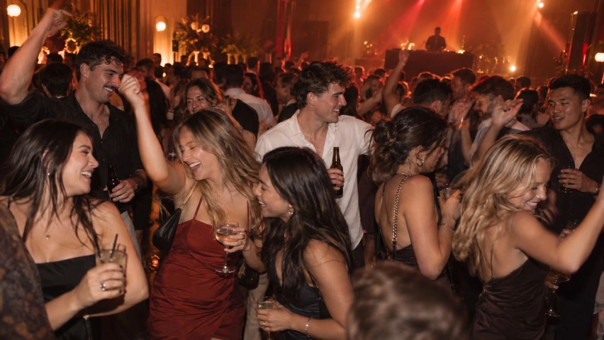 DJ hire in Sydney: a packed dance floor of guests laughing with drinks in hand, the DJ lit behind them
