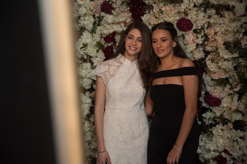 Two guests in formalwear photographed at the mirror booth flower wall at a Sydney event