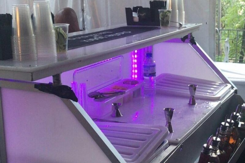 Bar top set with spirits, tools and ice under purple LED before service