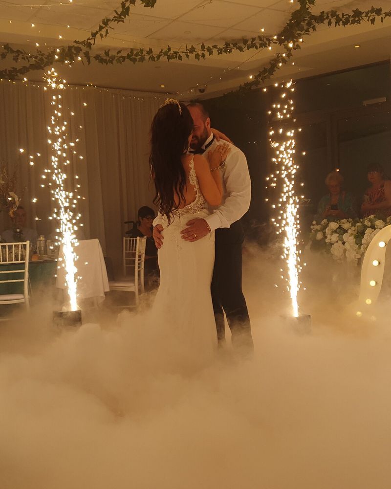 Bride and groom dancing in a low dry-ice cloud between two cold sparkler fountains