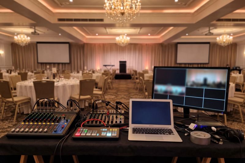 Illustration of an audio mixing desk, video switcher and laptop at the back of a gala dinner ballroom with two projection screens