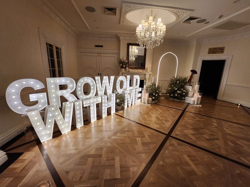 Illuminated GROW OLD WITH ME marquee letters under a chandelier