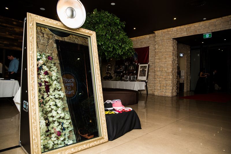Gold-framed mirror booth set against a white flower wall with a props table in a stone-walled Sydney venue