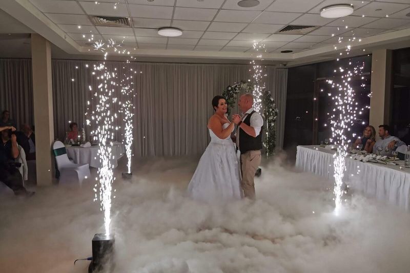 Bride and groom framed by sparkler fountains with cloud across the floor