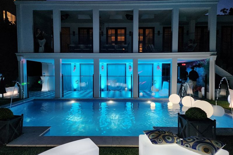 Poolside party set-up lit blue at night with white lounge furniture
