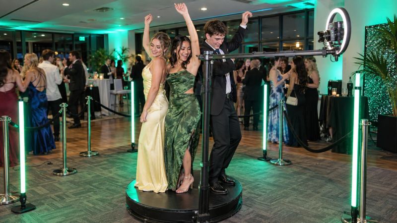 Guests in formal wear posing on a 360 booth platform between green LED light poles