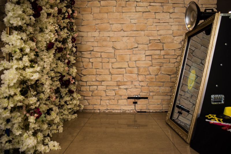 Retro mirror booth on its easel beside a flower wall and exposed brick