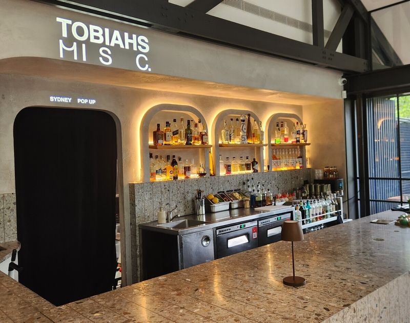 Venue name projected in light above the back bar at a Sydney pop-up, with the whole bar and lit shelving in frame