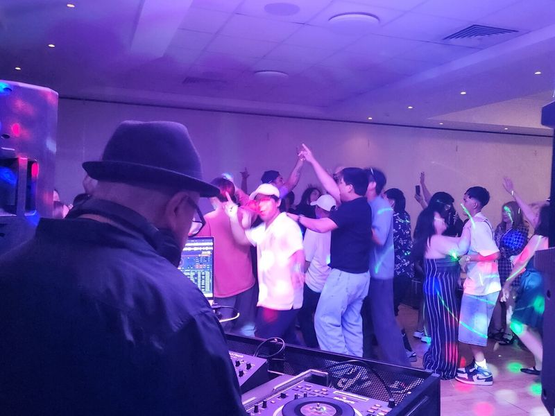 View from behind the DJ across a packed dance floor with guests' hands in the air