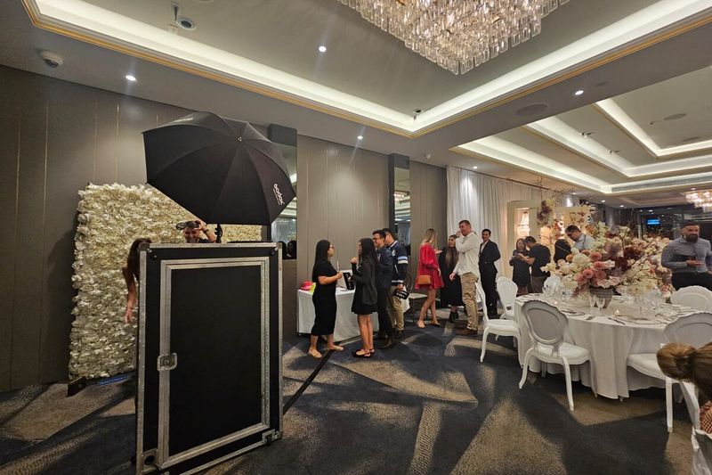 Mirror booth and white flower wall in a chandeliered ballroom with guests at the tables